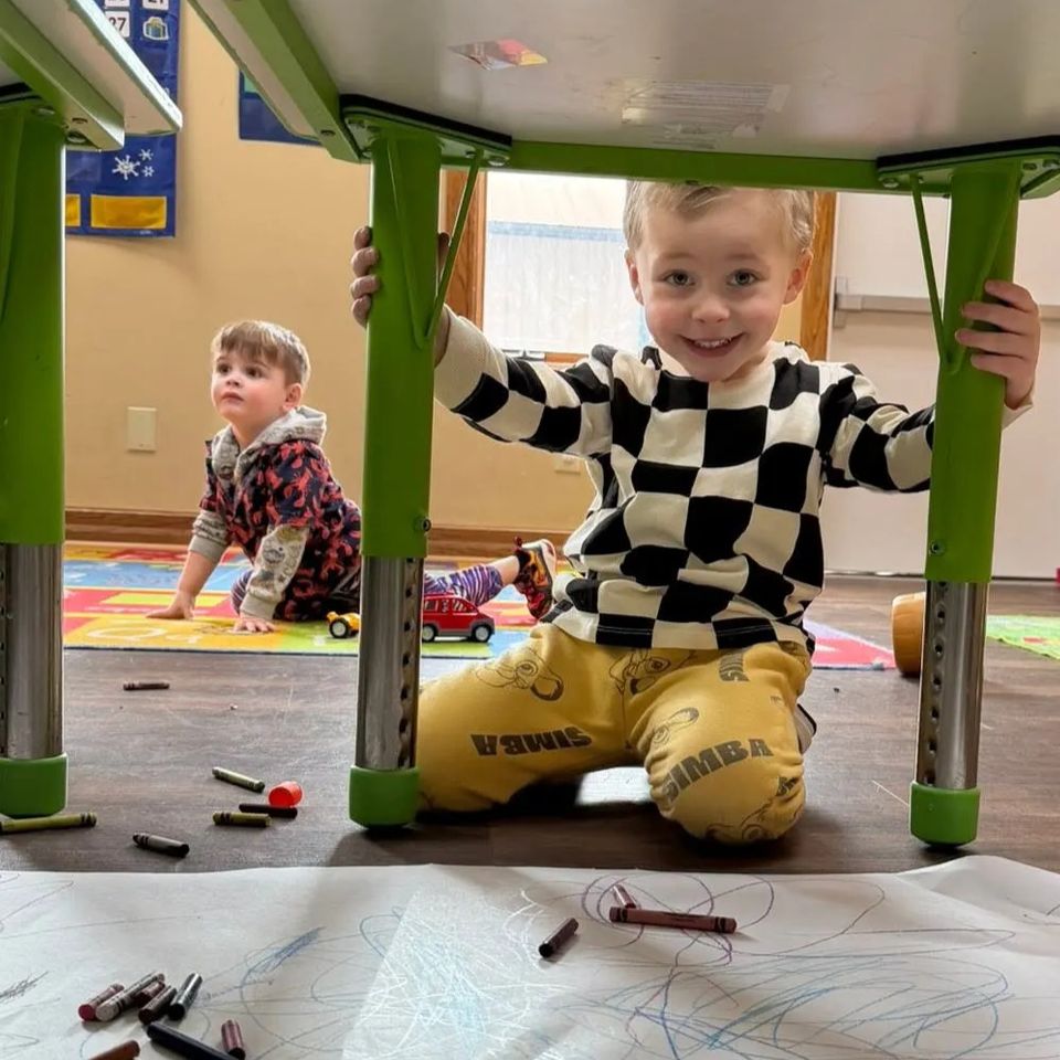 Two toddlers playing under a table