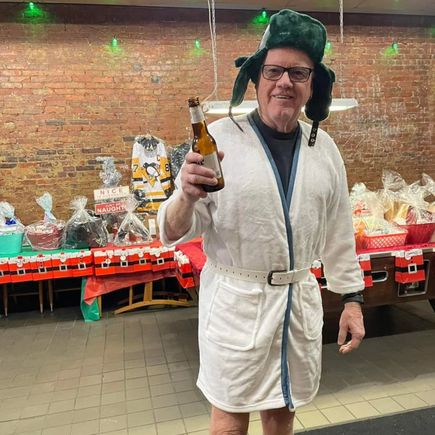 Attendee wearing a festive robe and winter hat holding a drink during a holiday-themed event.