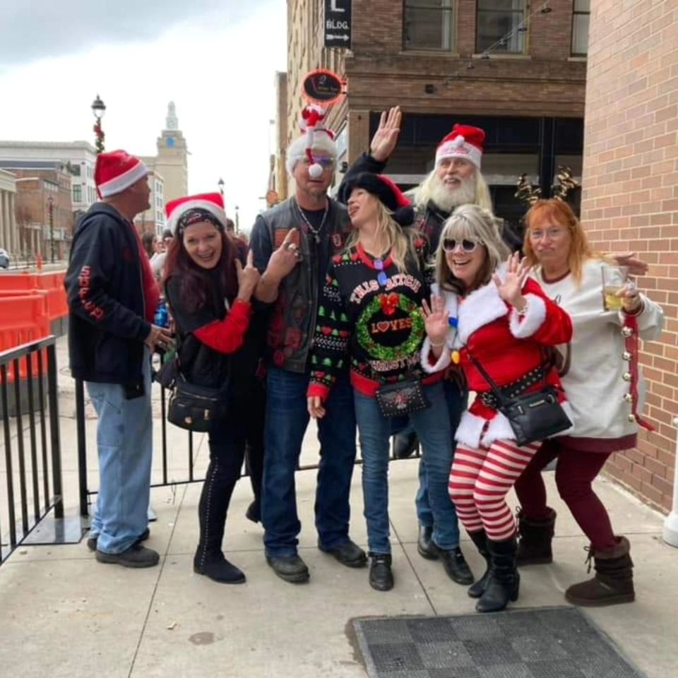 Group of attendees in festive Christmas outfits posing together outside during a holiday event.