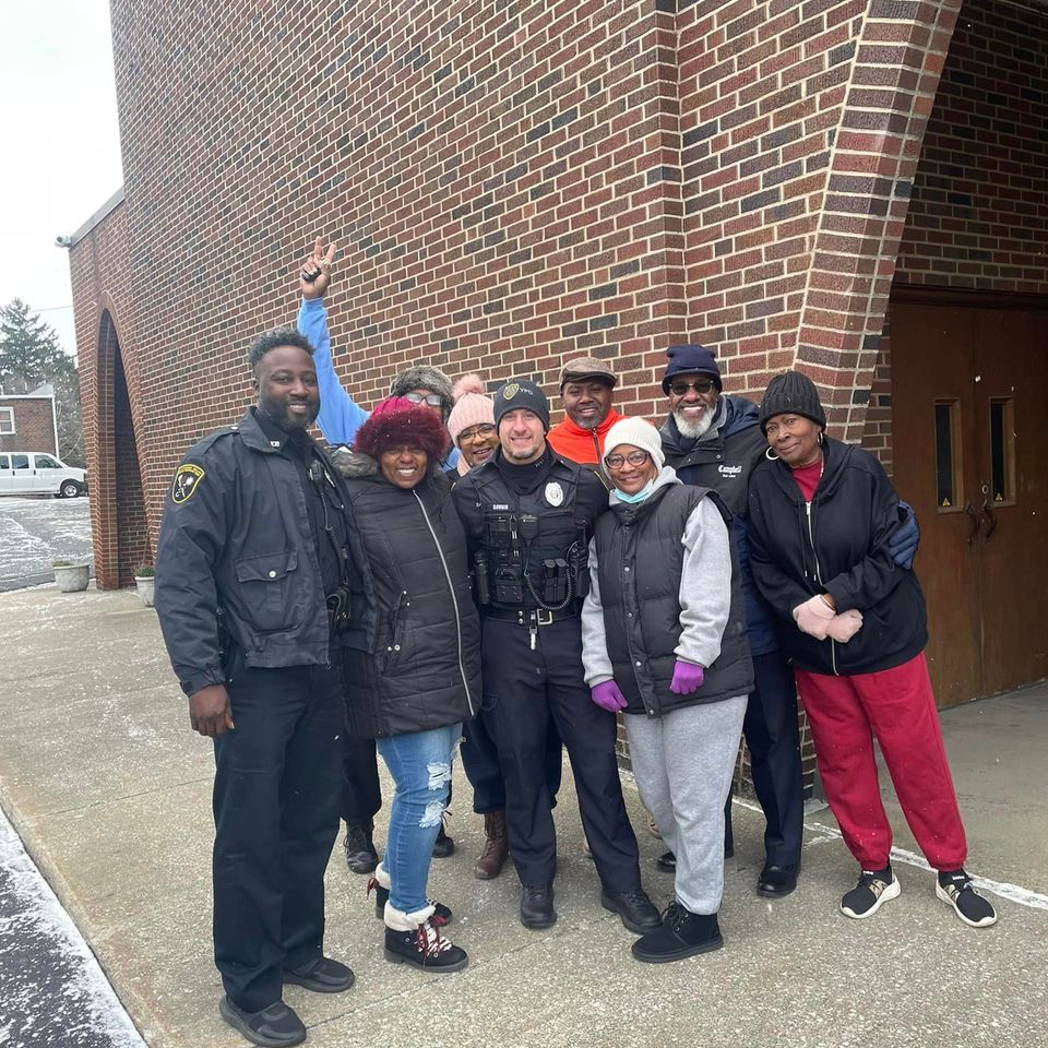 Group photo of church members and local officers gathered outside Grace Evangelistic Temple Church near the main entrance.