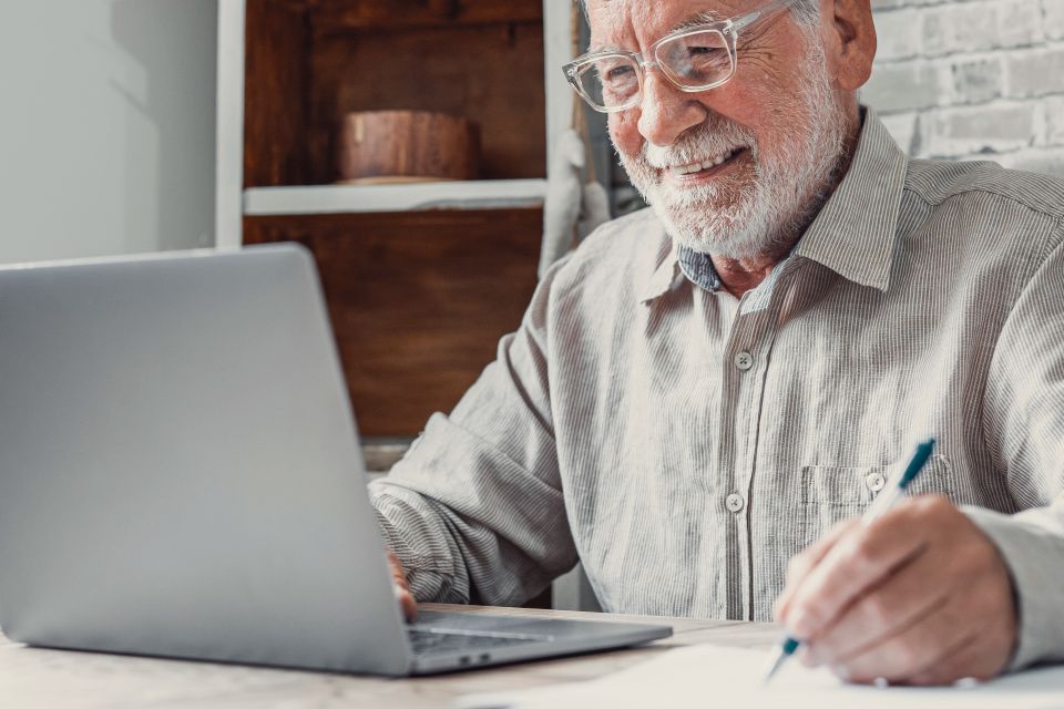 Senior man smiling while working on laptop and taking notes during senior care seminar on Long Island NY