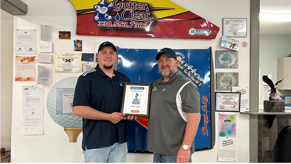 Gutter Clear LLC team member holding an award plaque inside the company office surrounded by company recognitions and certifications.