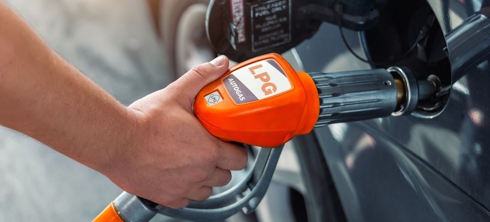 Man refueling car with orange LPG pump at gas station, demonstrating the use of propane as an alternative fuel.