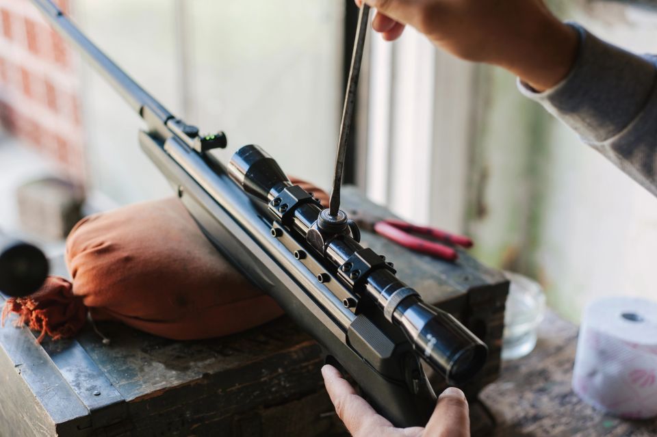 The gunsmith adjusts the optical sight of the sport air rifle. Adjusting the sniper rifle at a distance