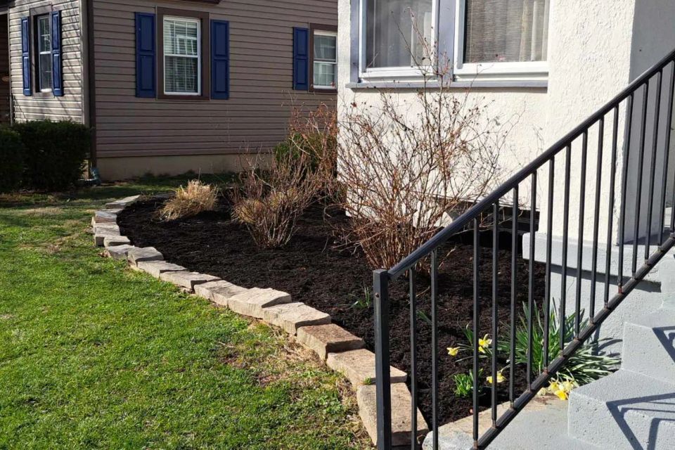 Front entry landscape featuring black mulch, flowering plants, and decorative stone borders.