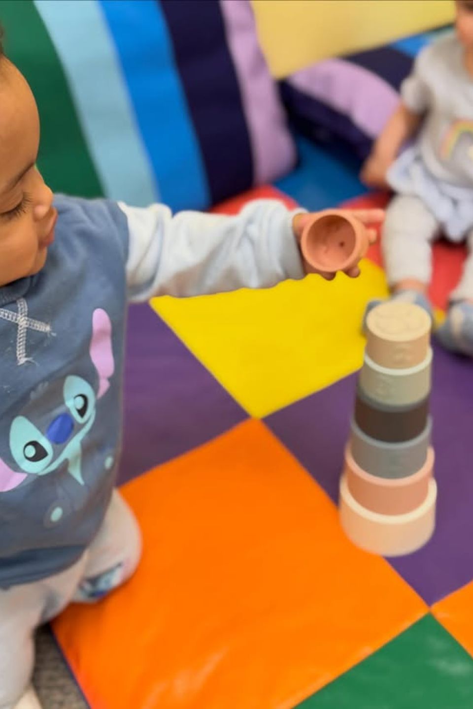 Toddler stacking nesting cups on a colorful play mat during infant daycare activities in Palmdale CA