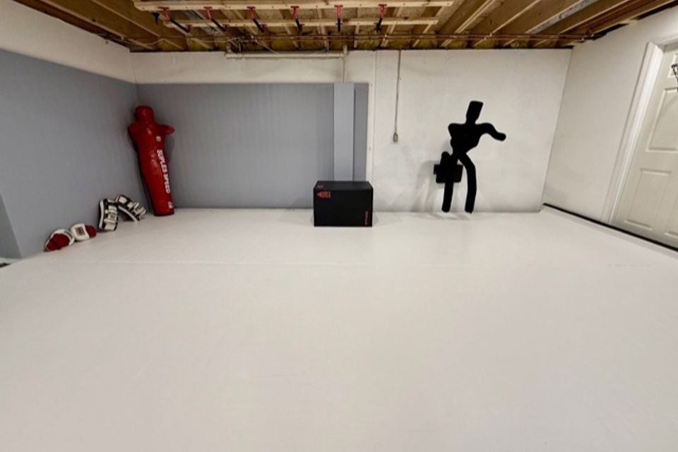 Wide view of white training mats, grappling dummy, and striking pads in an Okemos private martial arts studio