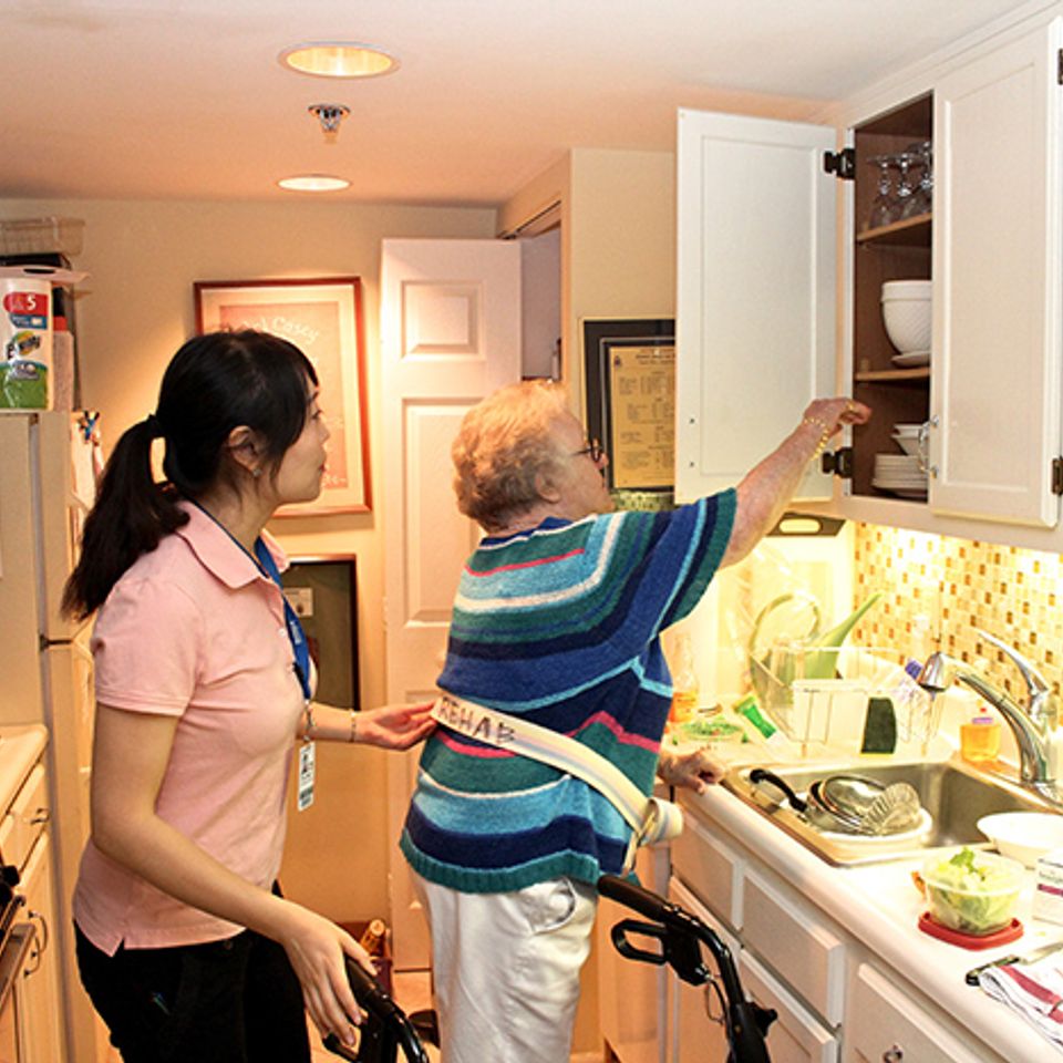 Female senior reaching to shelf in kitchen with ot fall prevention belt skilled nursing facility