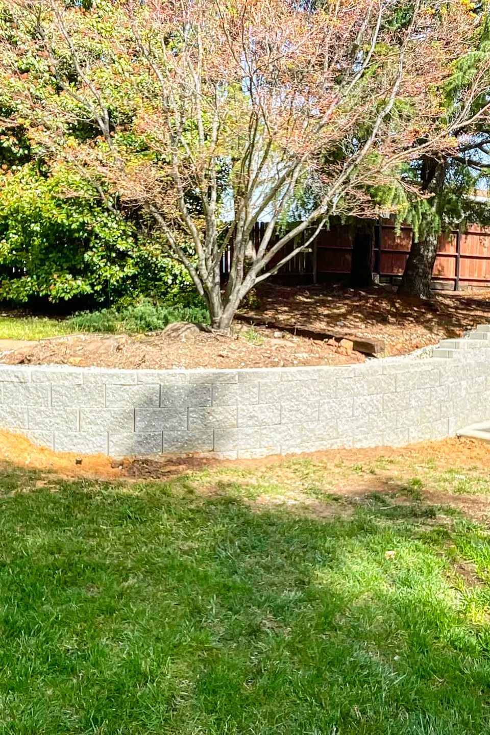 Completed luxury backyard remodel by Alta Vista Landscaping & Tree Service featuring a custom stacked stone fire pit, stamped concrete patio, and a tiered block retaining wall with integrated seating in El Dorado County