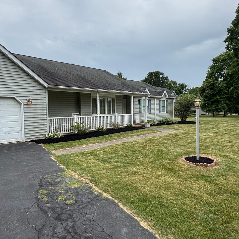 Front view of a single-story home with fresh black mulch, trimmed shrubs, foundation plants, and a neatly maintained lawn.