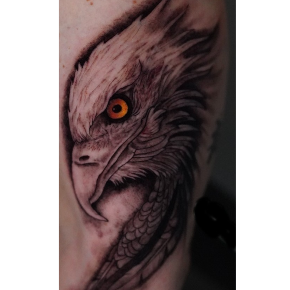 Image of an eagle tattoo in black and grey except the eye id golden with a mesmerizing black pupil