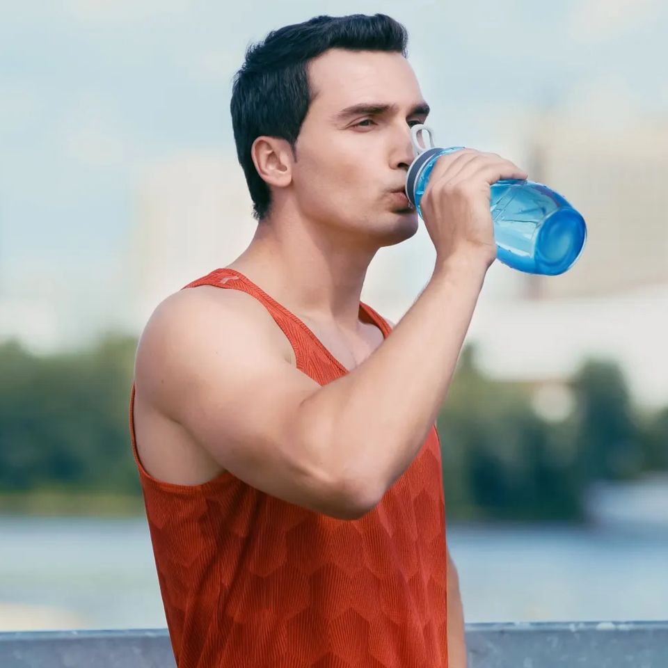 Man in an orange tank top drinking water outdoors after Quench electrolyte hydration IV therapy in Palm Beach County FL