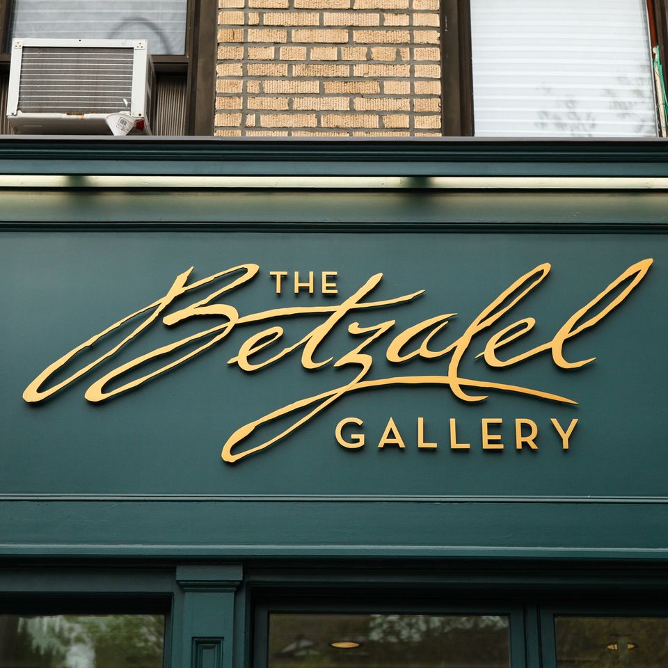 Gold script and block dimensional letters on a dark green storefront panel, lit by a cove light above