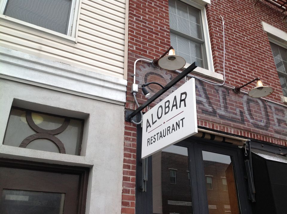 White rectangular blade sign on a black bracket with gooseneck lights above a restaurant entrance