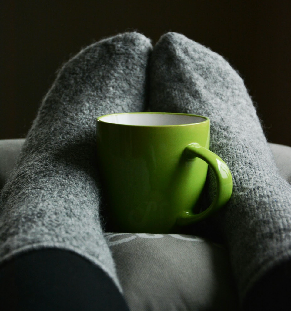 Person wearing gray socks cradeling a lime green mug