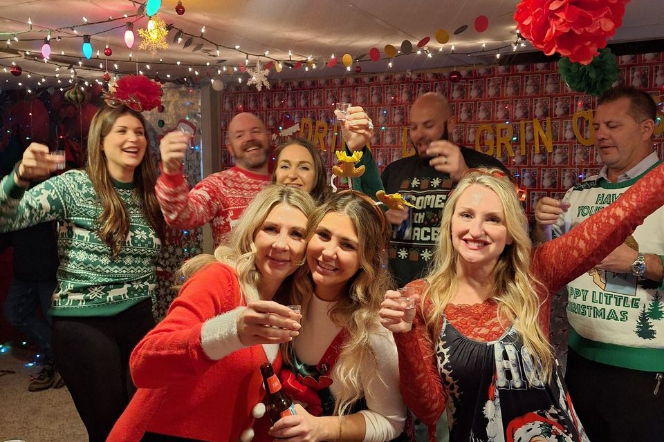 Group of guests in Christmas attire raising drinks and smiling at a holiday gathering