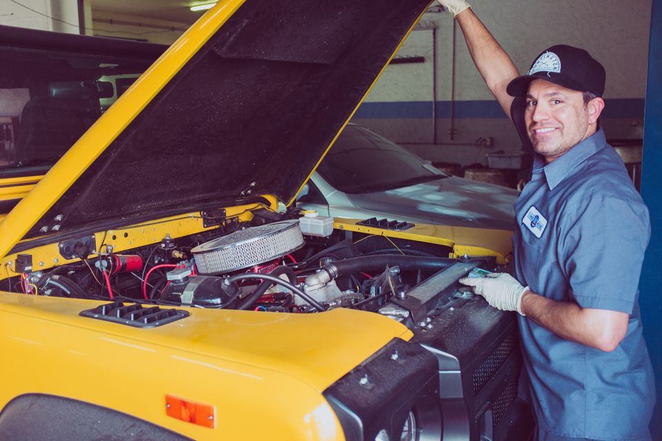 Image of a mechanic opening the hood on a yellow car.