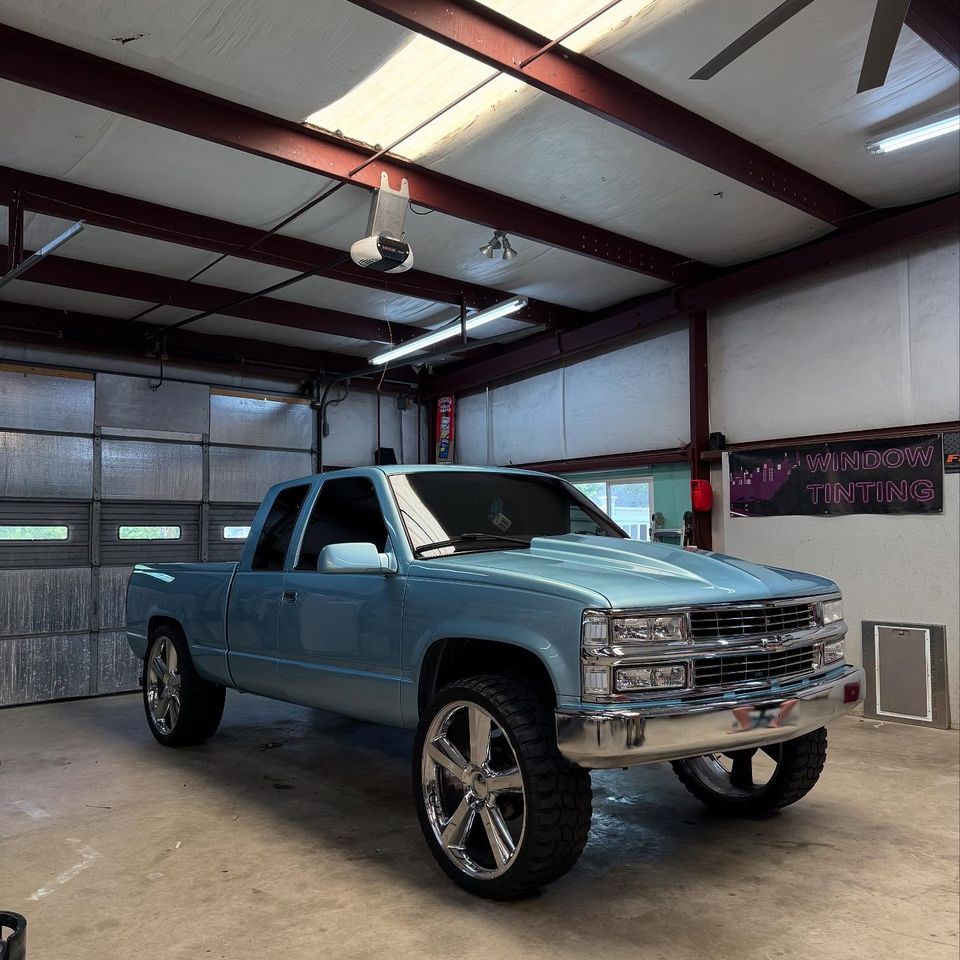 Light blue lifted Chevrolet extended cab truck on chrome wheels in the shop for window tinting