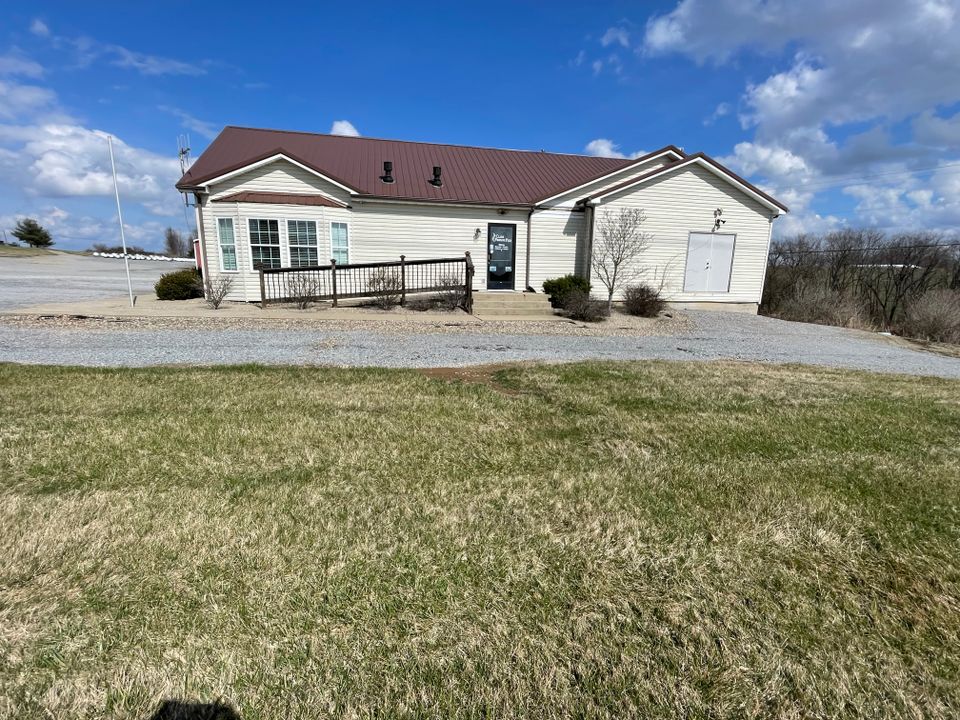 Clark Propane Plus Flemingsburg with a brown roof and beige siding, surrounded by grass, gravel pathways, and a clear blue sky with a few clouds.