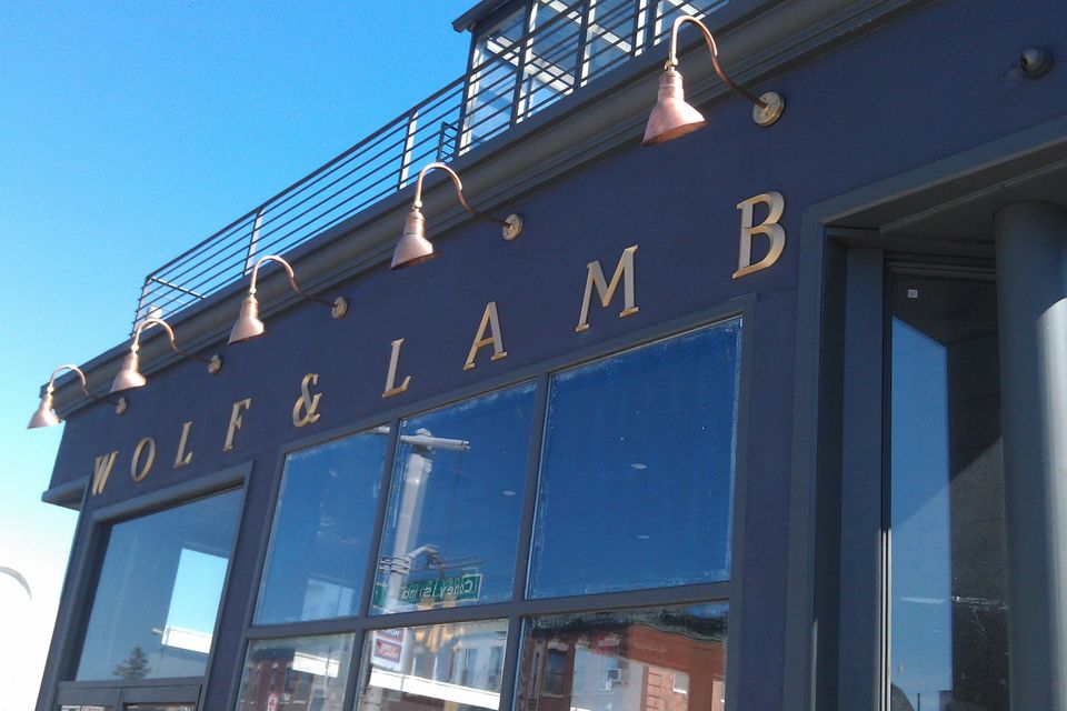 Gold pin-mounted serif letters spanning a dark navy storefront facade beneath copper gooseneck lights