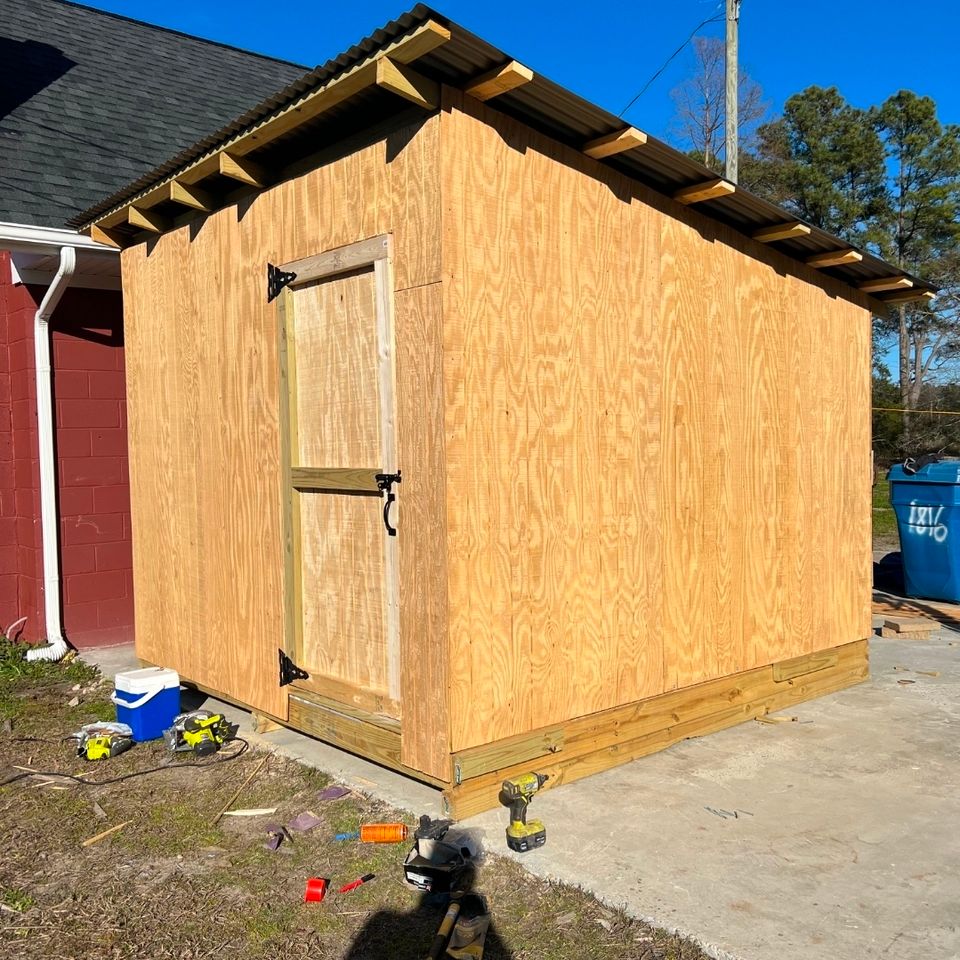 New plywood storage shed with metal roof under construction beside brick building in Virginia Beach VA