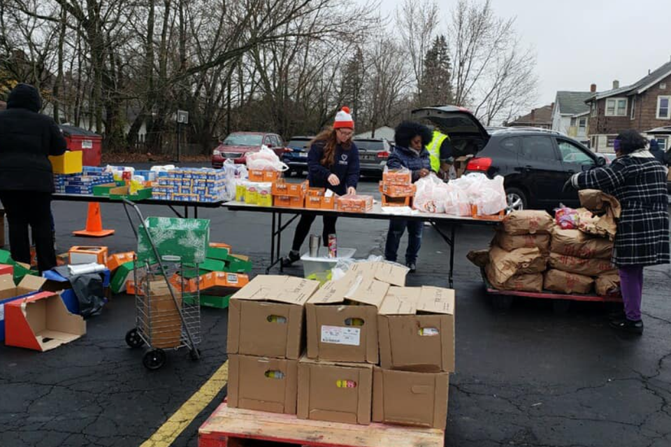 Volunteers organizing and distributing food boxes, groceries, and household supplies during a community assistance program in a church parking lot.
