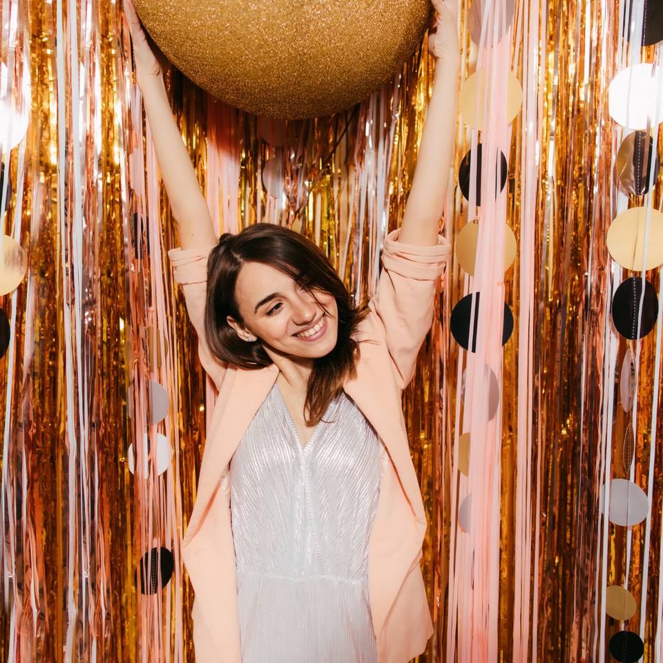 Woman posing in front of a shimmering gold and pink photo booth backdrop.