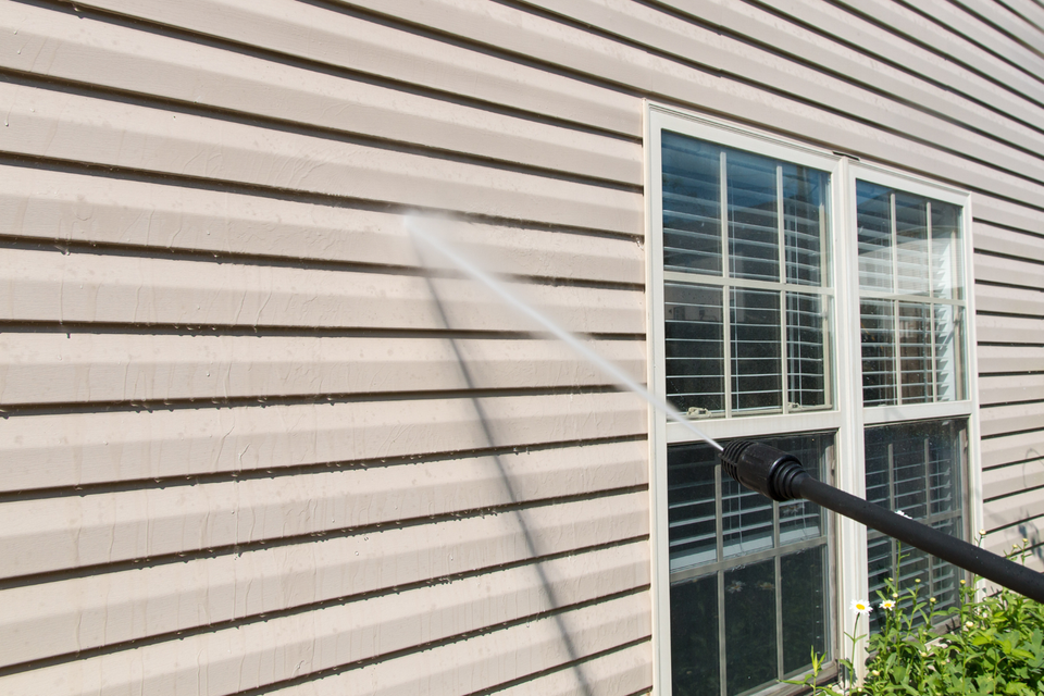 Pressure washing the siding of a residential home as part of a professional house cleaning service.