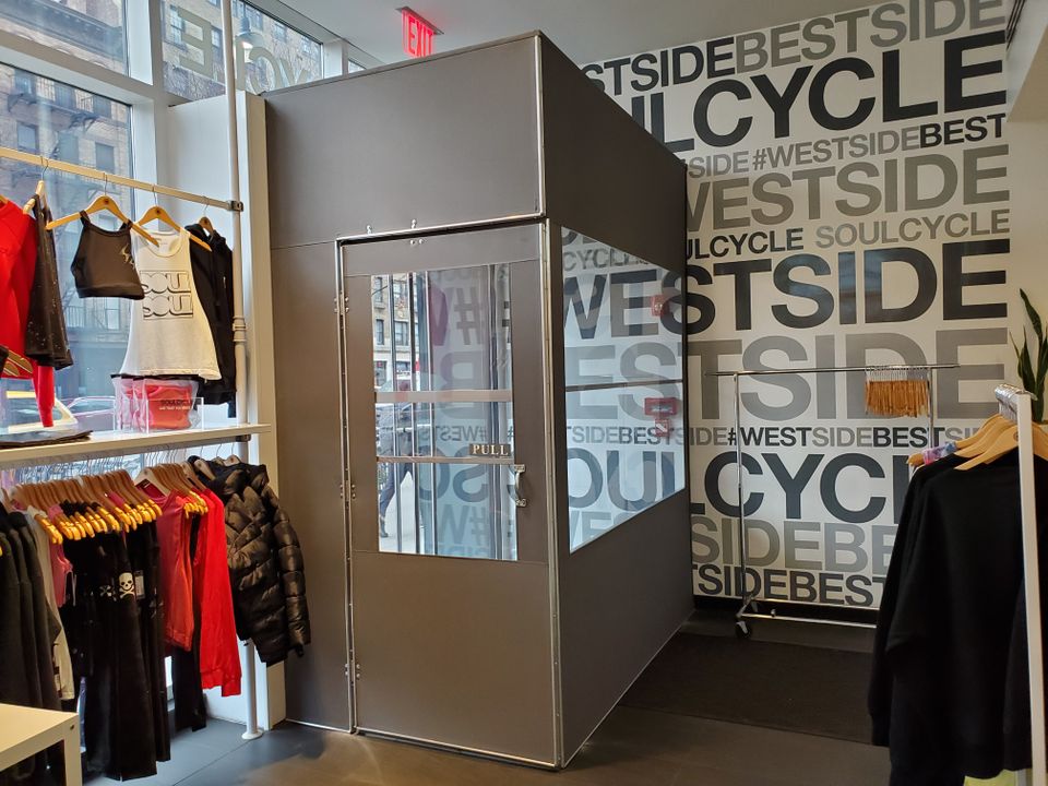 Brushed aluminum vestibule with a glazed door built inside a retail store entrance, photographed from the sales floor