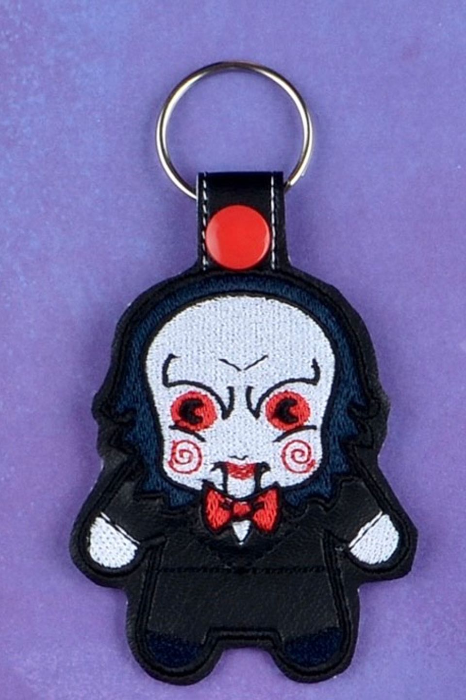 Custom embroidered horror puppet keychain with black suit, red bow tie, and red spiral cheek details.