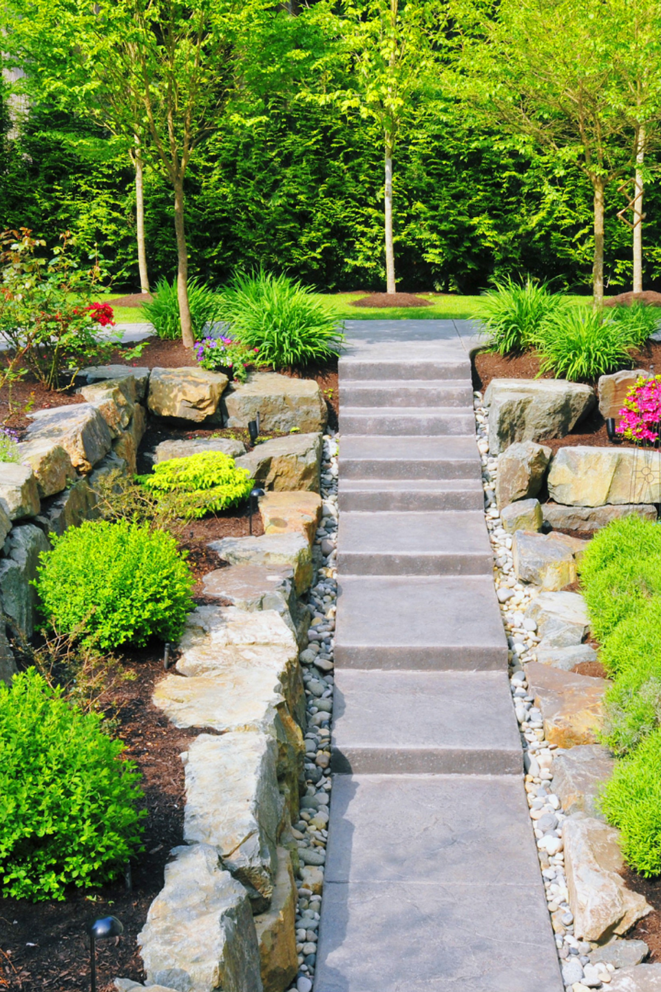 Custom residential landscape featuring natural stone retaining walls, concrete steps, ornamental shrubs, flowering plants, and professionally designed landscaping by R.E.P. Companies.