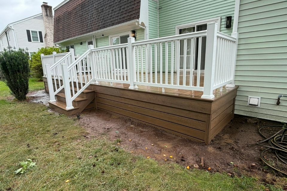 Composite deck with white vinyl railings and stairs behind green home in Virginia Beach VA