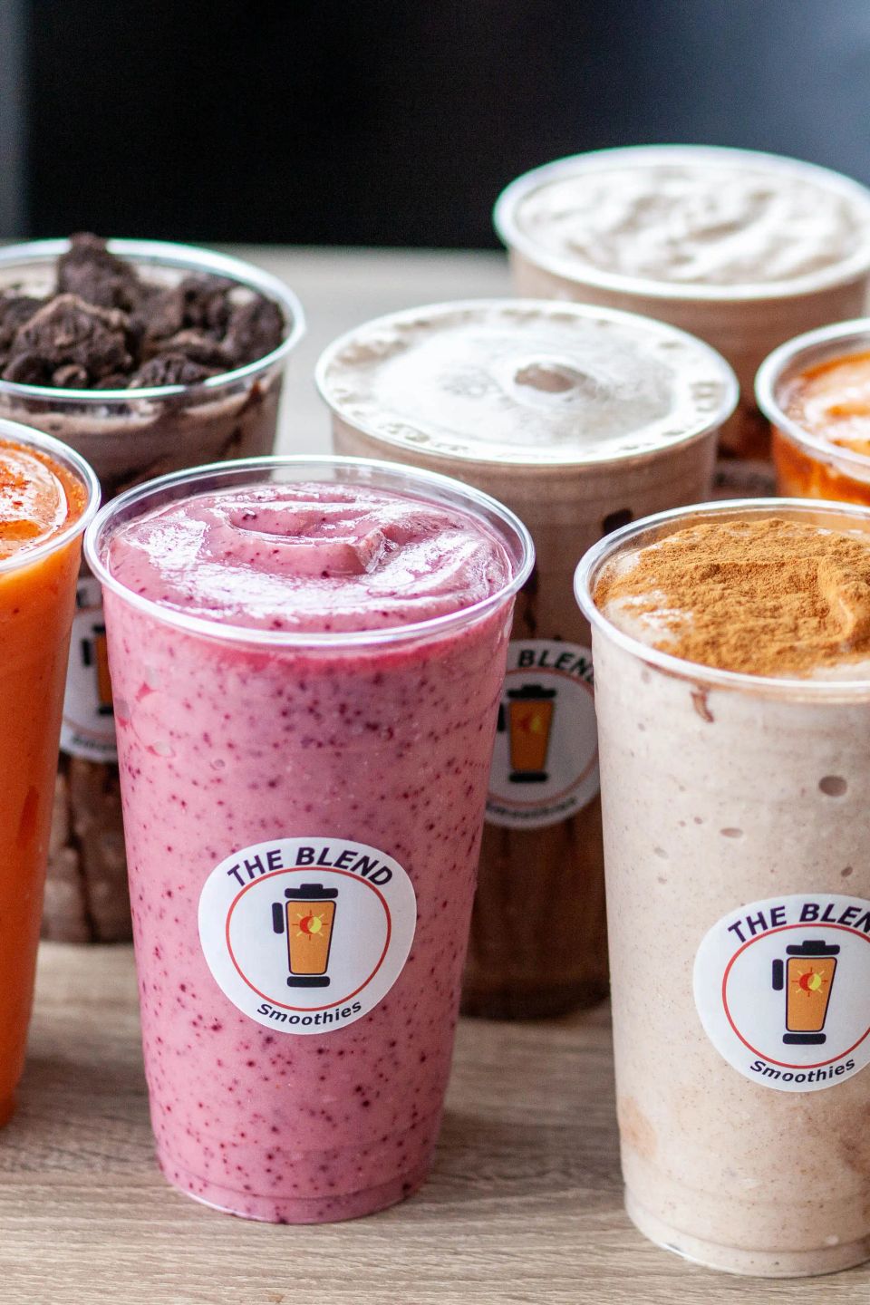 Assorted fruit and protein smoothies in branded cups from The Blend Smoothies, featuring berry, cinnamon, and chocolate flavors.