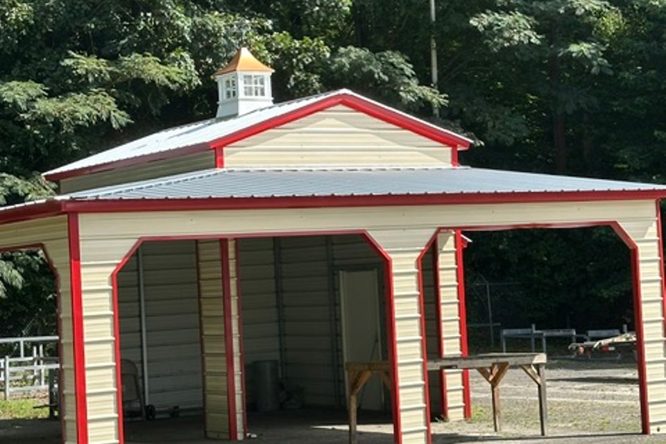 Tan and red steel barn style carport with cupola and open bays representing steel carports in Alabama