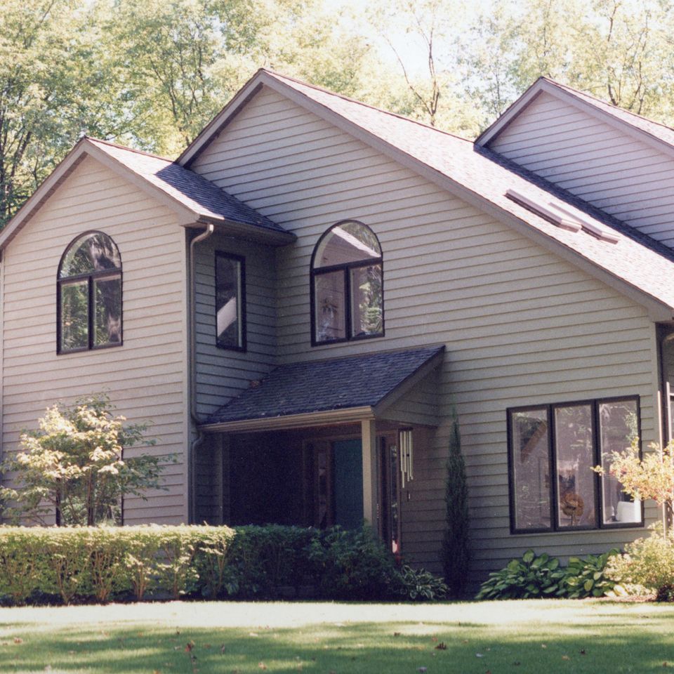 Two-story custom home featuring gray siding, large arched windows, landscaped yard, and mature trees.