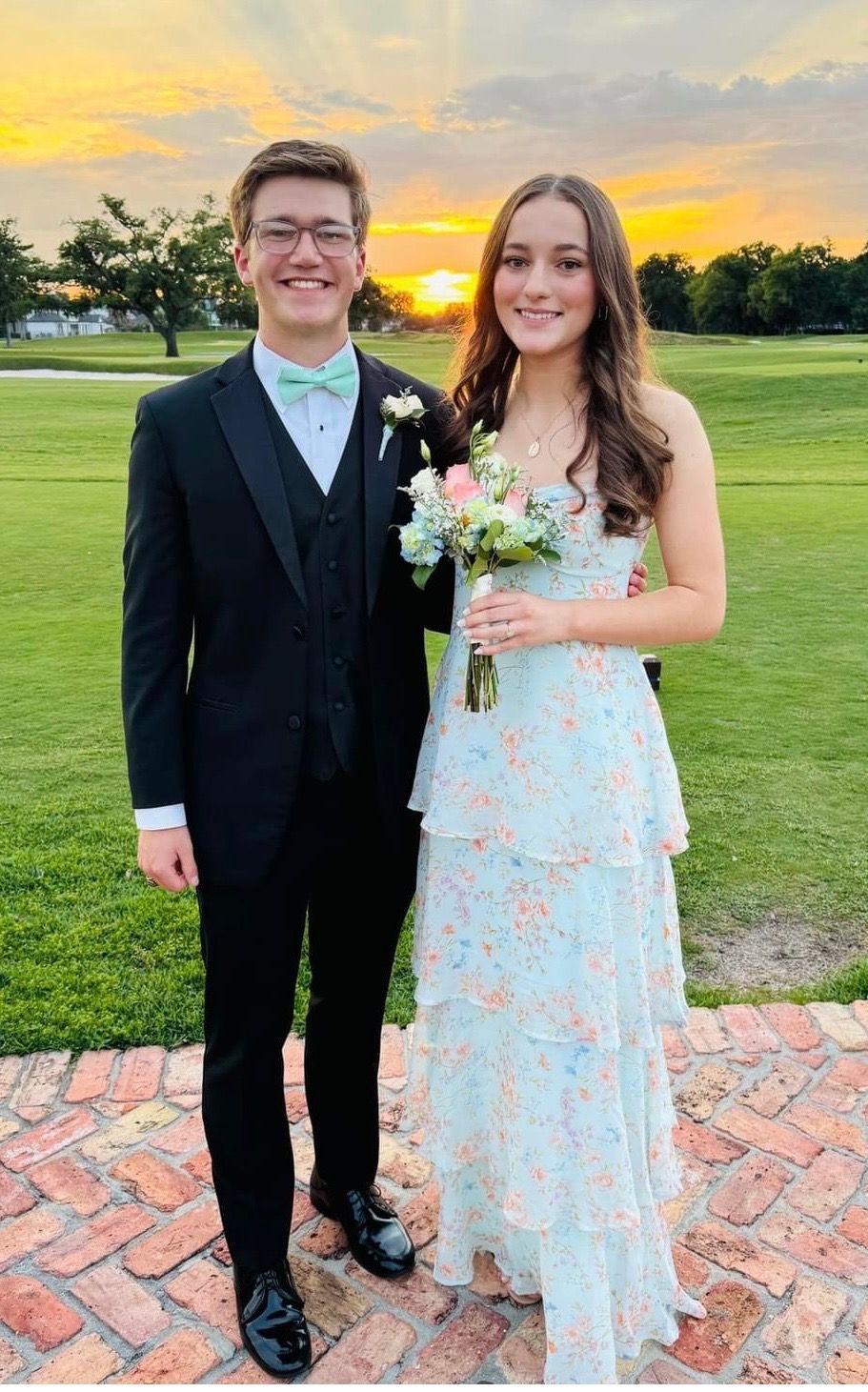 Prom couple posing at sunset, featuring a young man in an affordable black tuxedo rental with a mint green bow tie from New Orleans Tuxedo Inc., part of the $99 tuxedo rental collection.