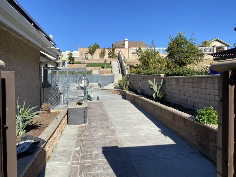 Backyard renovation with concrete walkway, retaining walls, planters, and outdoor living space