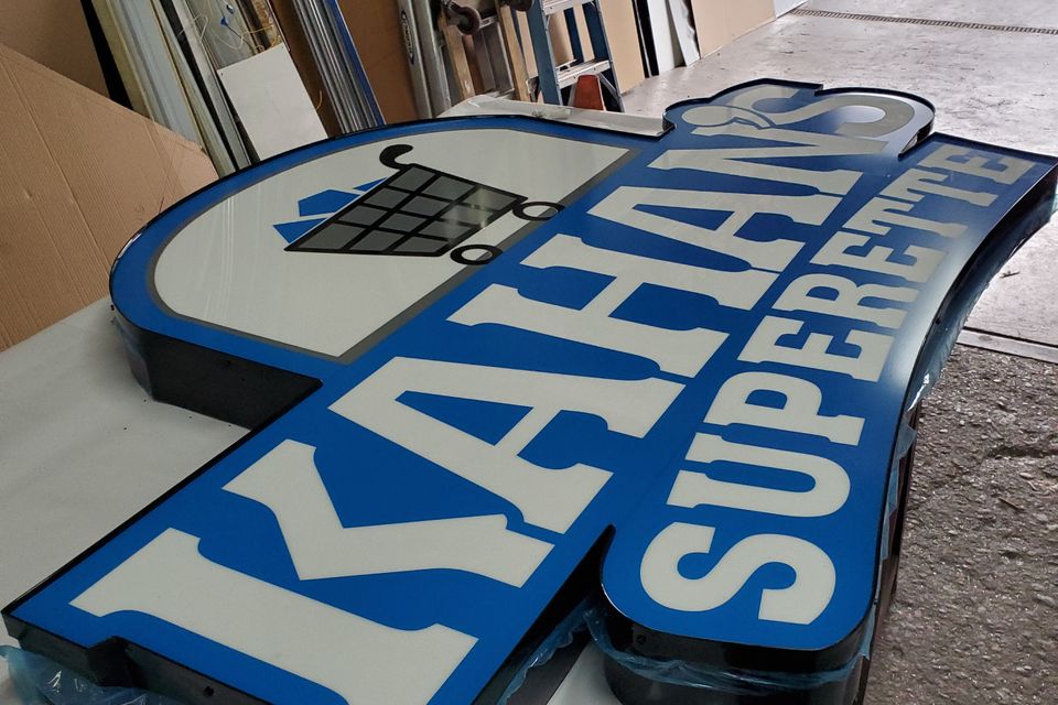 Custom shaped illuminated light box cabinet with a shopping cart graphic and routed lettering, finished and lying on the shop floor before installation