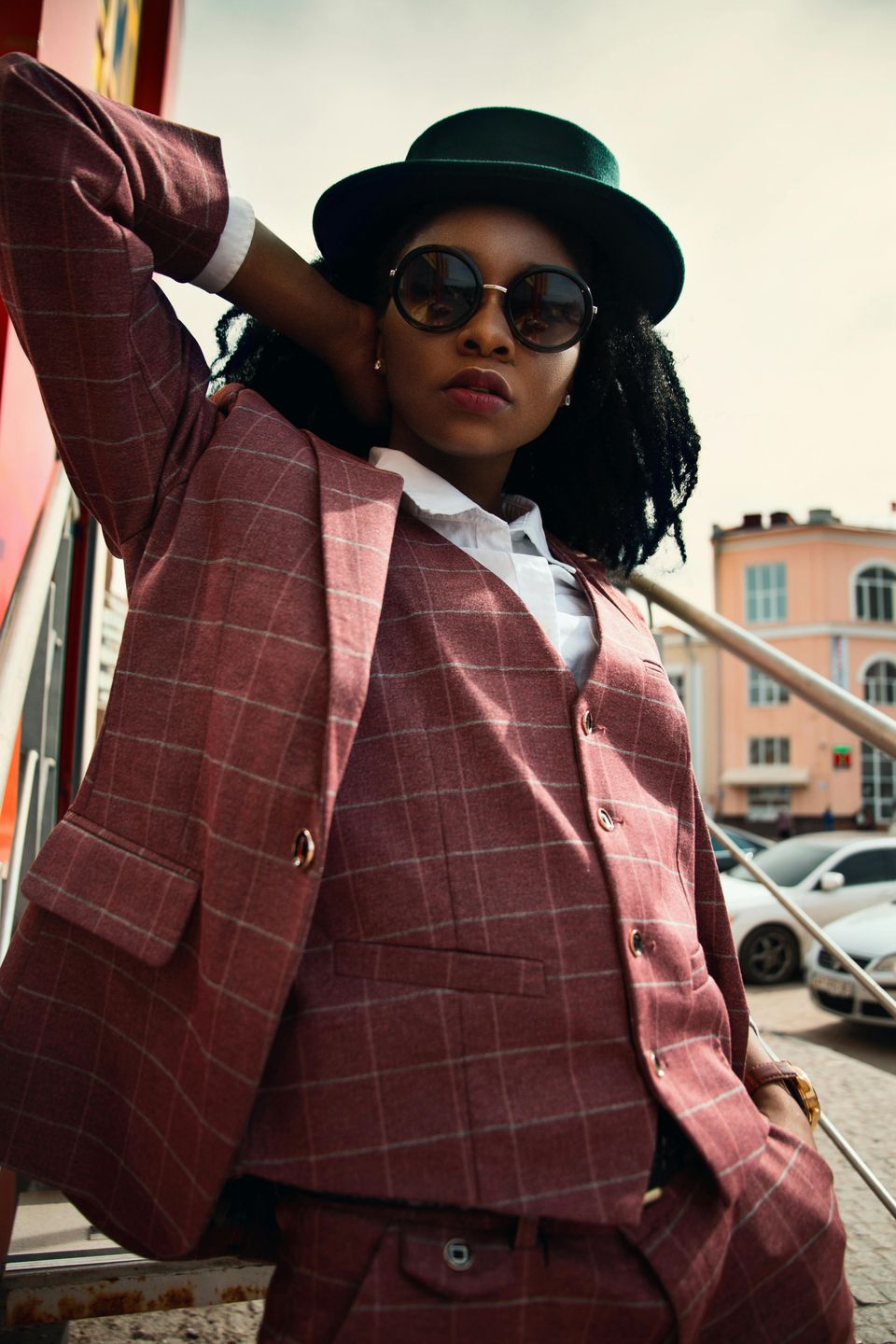 Black woman wearing sunglasses, black hat and maroon plaid suit.