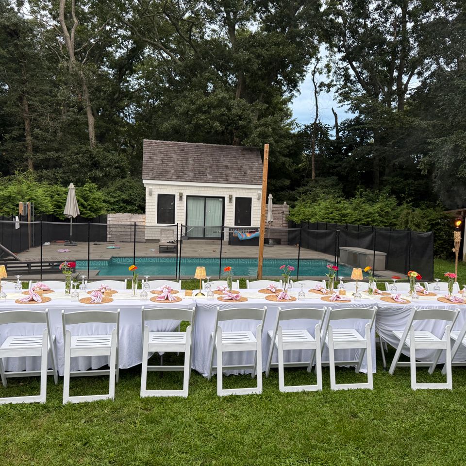 Long poolside banquet tables with pink napkins and zinnia bud vases in a Hamptons NY backyard