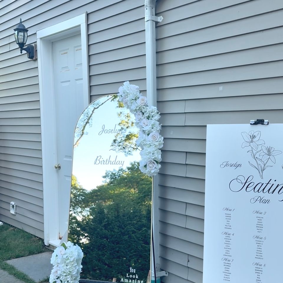 Floral-trimmed arched welcome mirror and seating chart styled for a backyard birthday in the Hamptons NY
