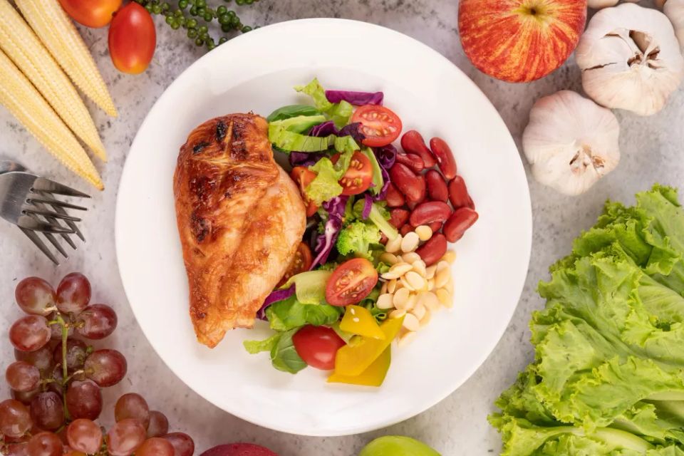 Chicken steak topped with white sesame peas tomatoes broccoli pumpkin white plate