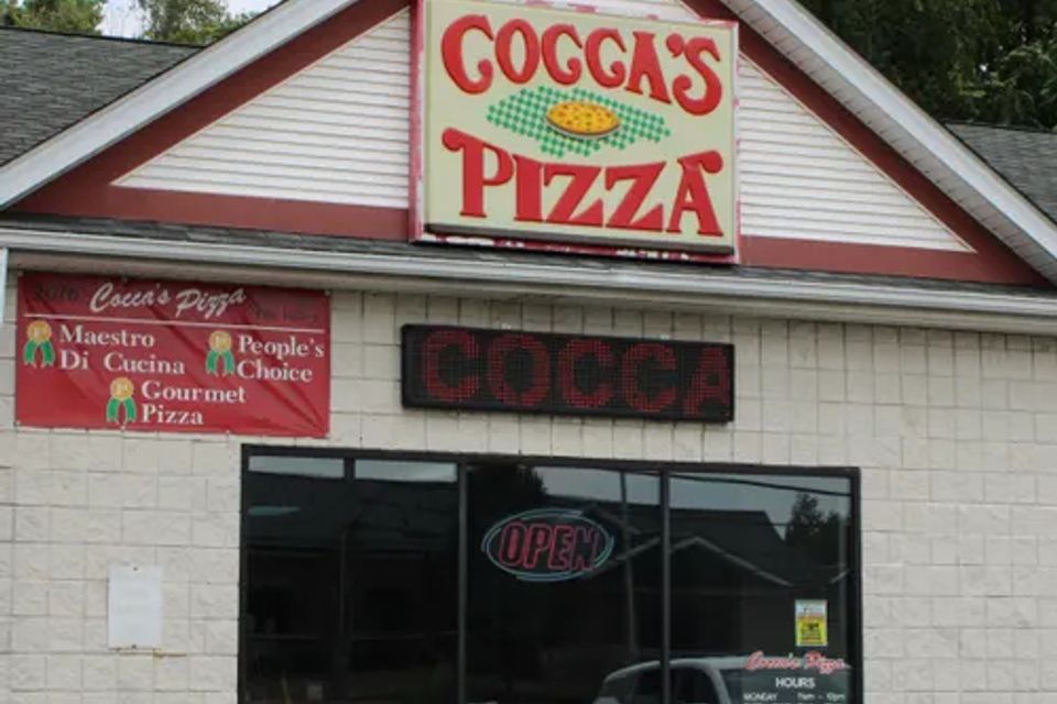 Cocca’s Pizza Liberty, Ohio storefront featuring a light-colored exterior, large front window, illuminated open sign, and prominent Cocca’s Pizza sign above the entrance.