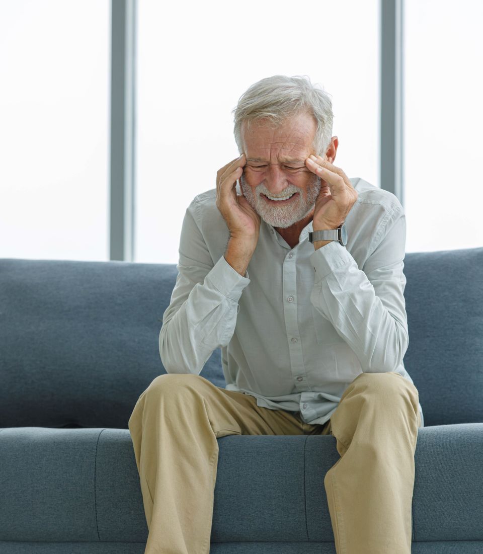 Old senior elderly unhealthy sick ill gray bearded and hair male grandfather sitting on sofa at home