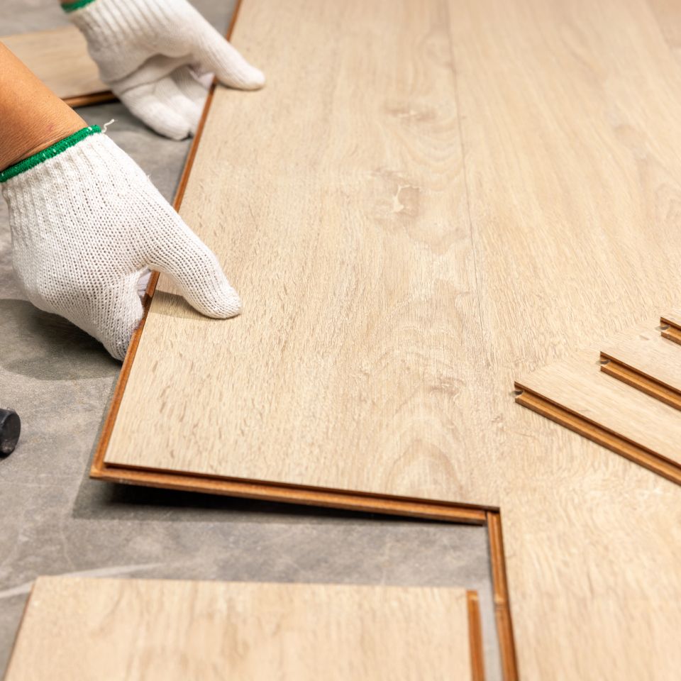 Gloved hands fitting light oak laminate floor planks into place