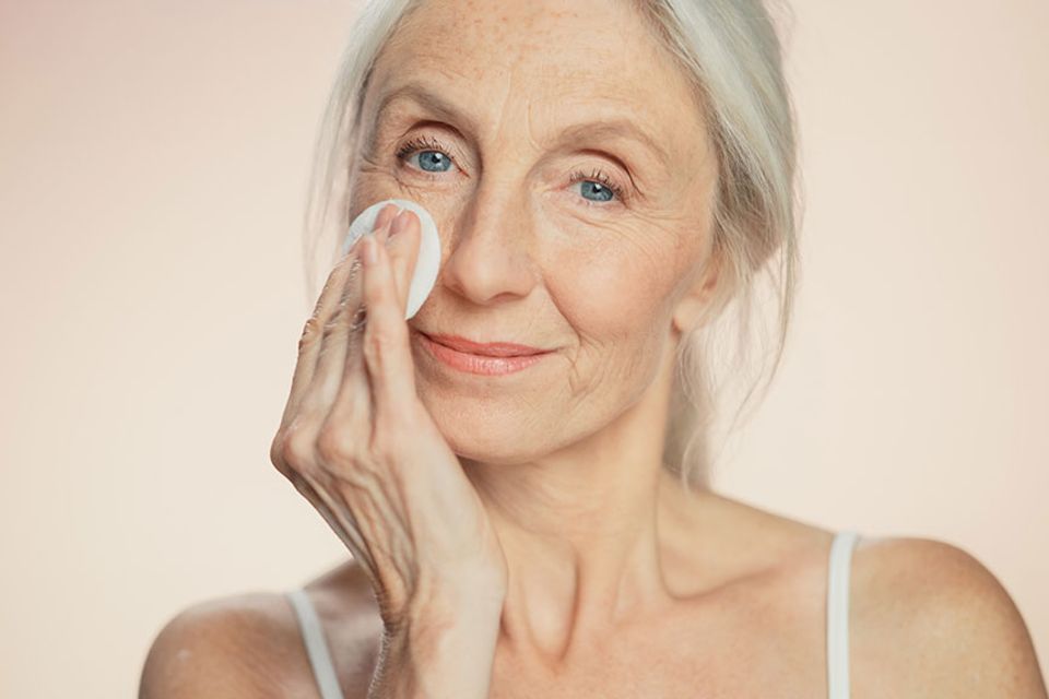 Beautiful senior woman uses cotton wool pad to clean her perfect face of cosmetics
