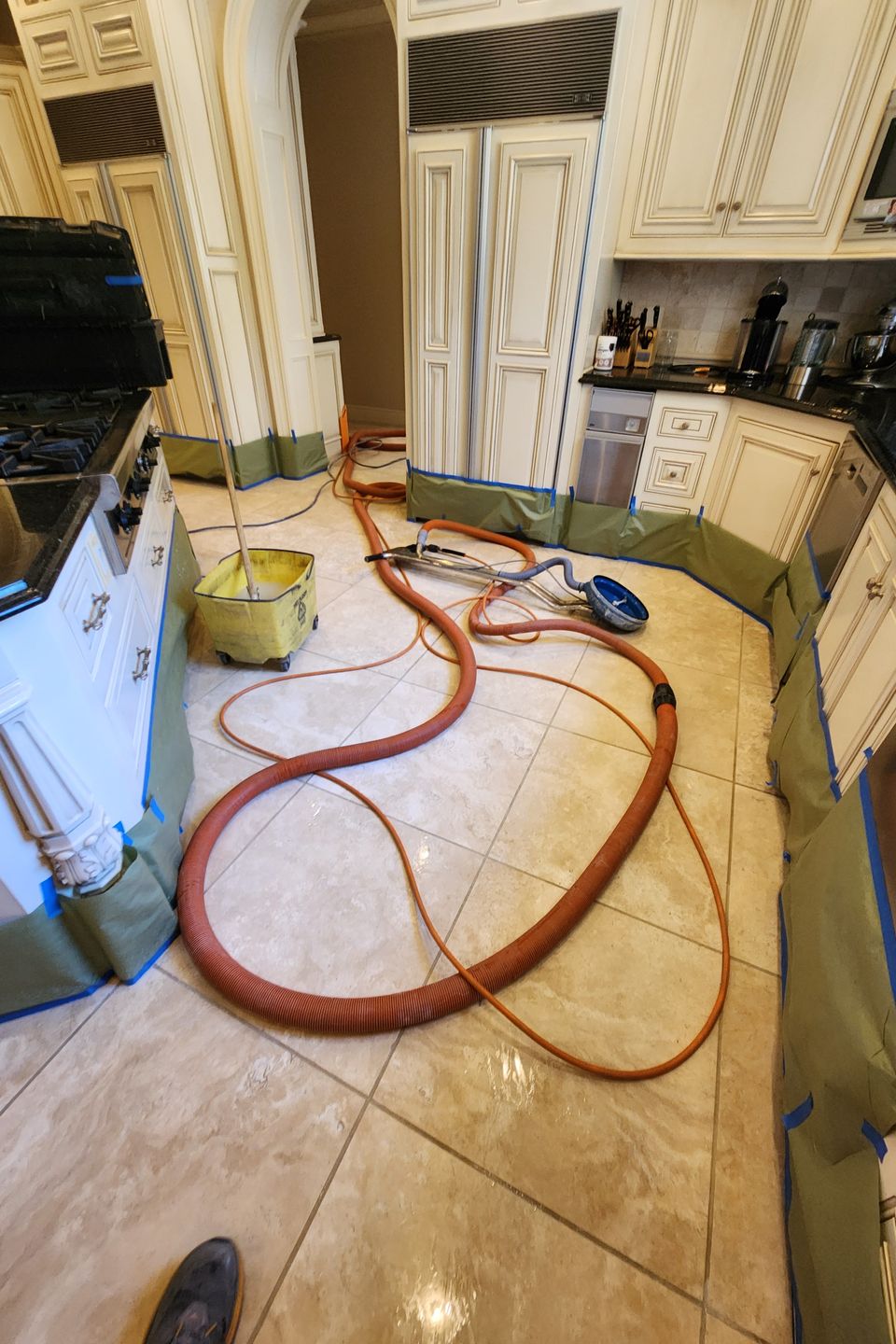 Kitchen with cabinets protected by green coverings, cleaning equipment and orange hose set up for restoration work