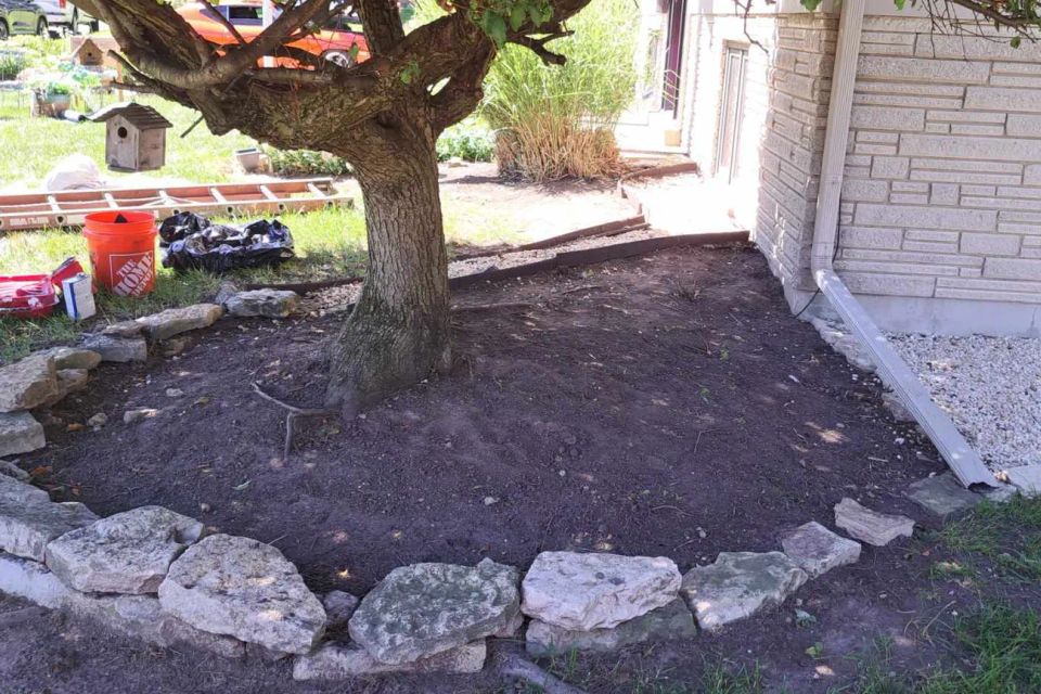 Landscape bed with natural stone edging surrounding a tree, prepared for mulch installation.