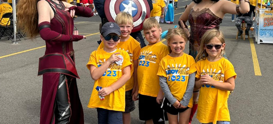Children wearing Buddy Walk shirts posing with superhero characters during the DSAV event.