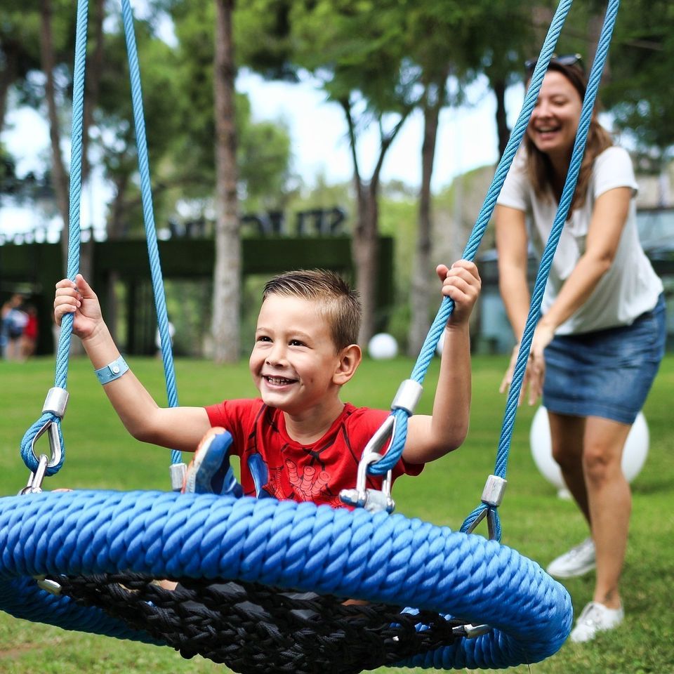 Smiling boy on a blue rope swing while an adult pushes him during outdoor playtime in Palmdale CA